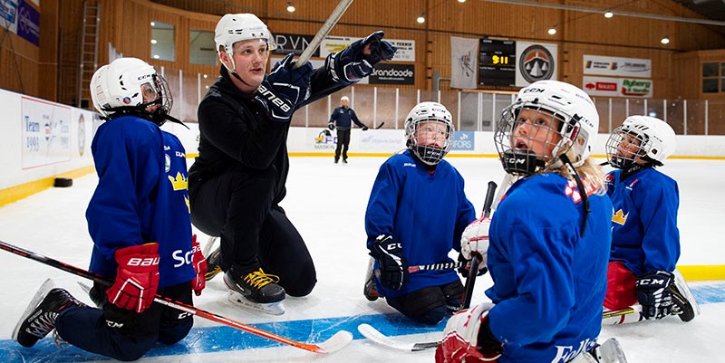 På en ishockeyrink pratar en ledare med några yngre barn