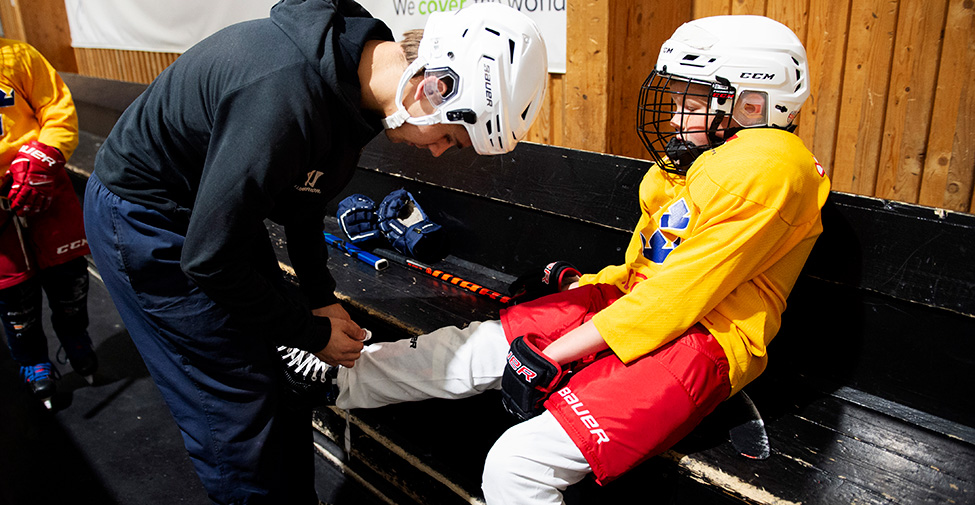 En ung ledare hjälper en hockeyspelare att knyta skridskorna. 