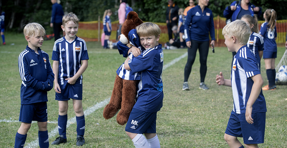 I en grupp av fotbollsspelande barn håller en pojke om en teddybjörn iförd matchtröja