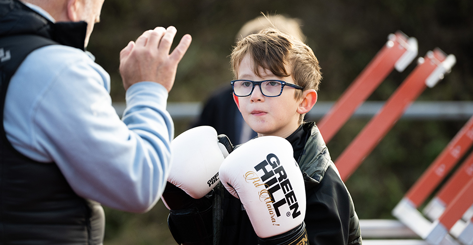 En pojke med glasögon, iförd ett par stora boxningshandskar